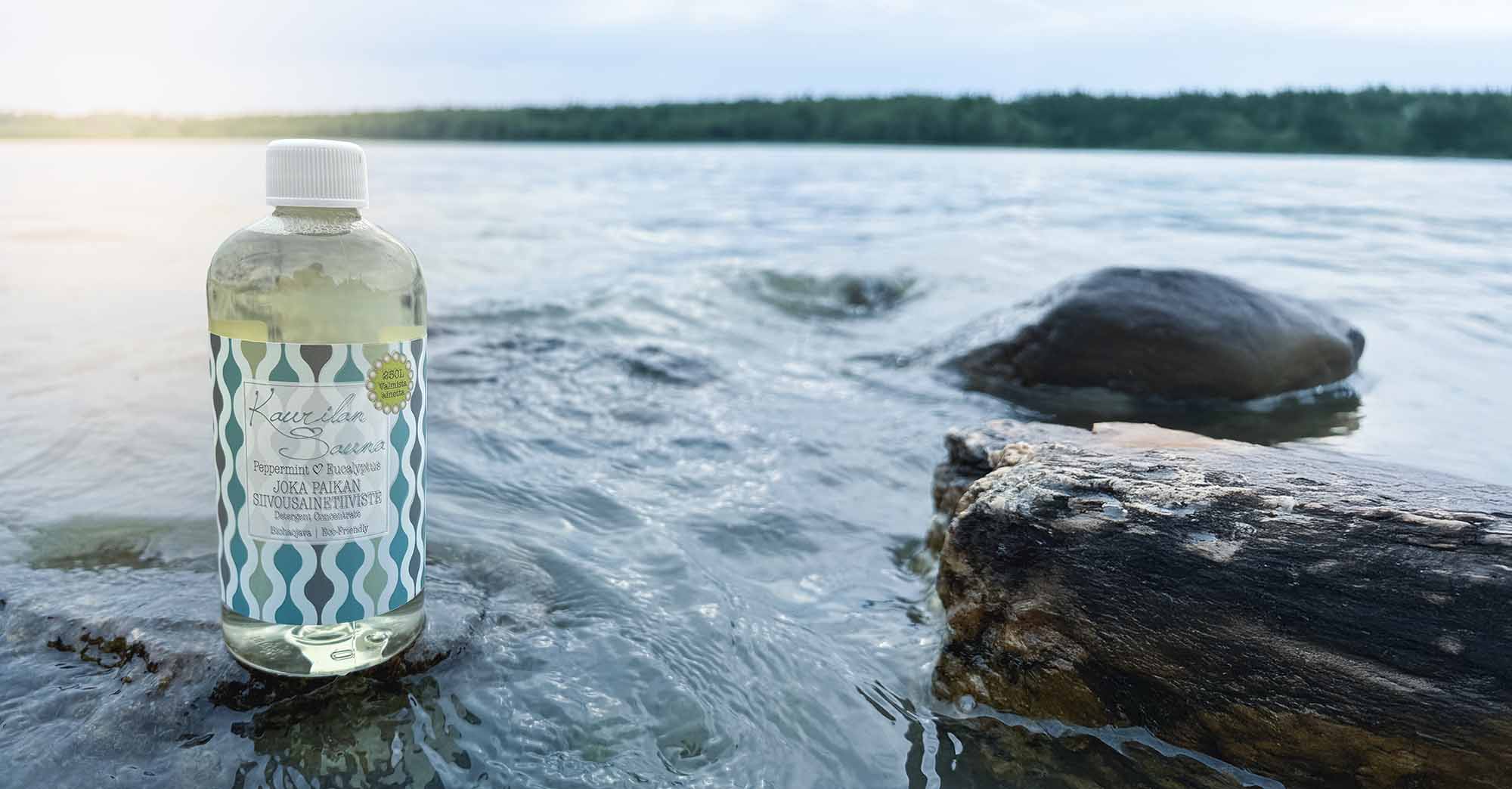 Siivousainepullo kesäillassa järven rannalla kiven päällä. 