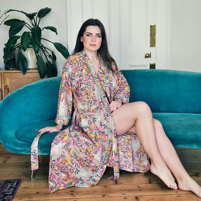 Powell Craftin Bird & Pomegranate -naisten puuvillainen kimonoaamutakki  tummahiuksisen turkoosilla sohvalla istuvan naisen yllä. 