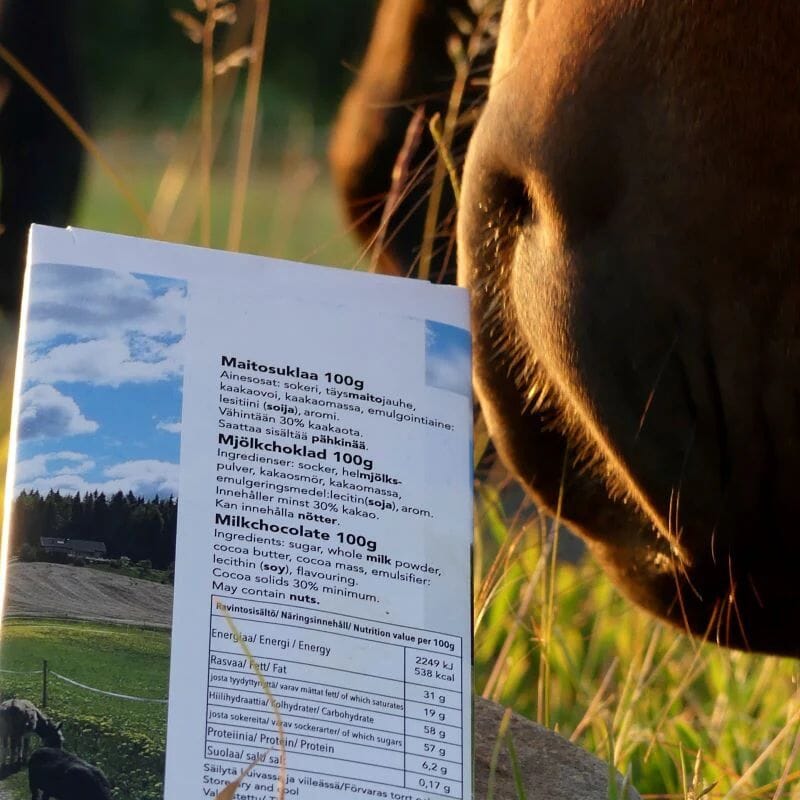 Tiluksilla Hyvän Mielen Maitosuklaa -pakkauksen takapuoli, jota nuuskuttelee hevonen. Pakkauksesta selviää maitosukslaan ainesosat ja ravintosisältö.