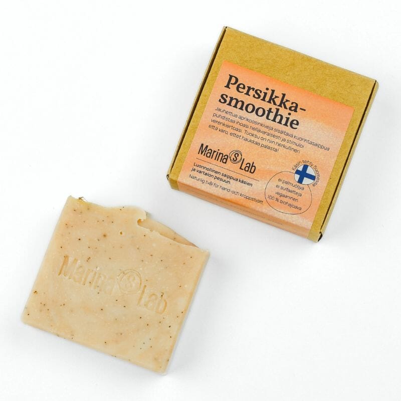 Marina's Labin kuoriva Persikkasmoothie- palasaippua ja sen kartonkipakkaus valkoisella taustalla. Saippua on kauniin persikkaisen sävyinen, samoin pakkauksen etiketti. 