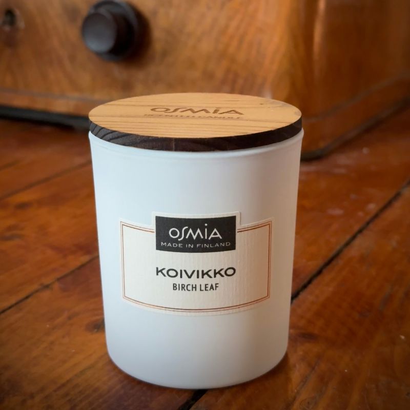 Osmian Koivikko -tuoksukynttilä raikkaan valkoisessa lasipurkissa puisella, ajan patinoimalla lattialla. Luonnonläheinen ja nostalginen tuoksu sopii lämpimään sisustukseen ja luonnonmateriaaleja suosivaan tyyliin.