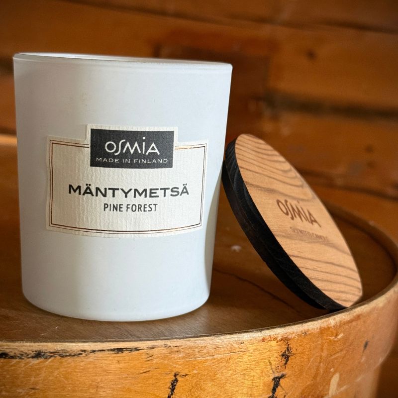 Osmia Tuoksukynttilä - Mäntymetsä valkoinen lasipurkki lepää kansi auki rustiikkisen puulaatikon päällä. 