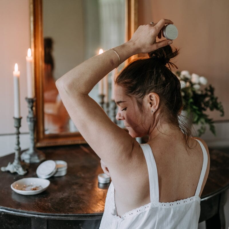 Kaurilan Saunan Saara levittämässä deovoidetta kainaloonsa mehiläisvahakynttilöiden ja peilin edessä.