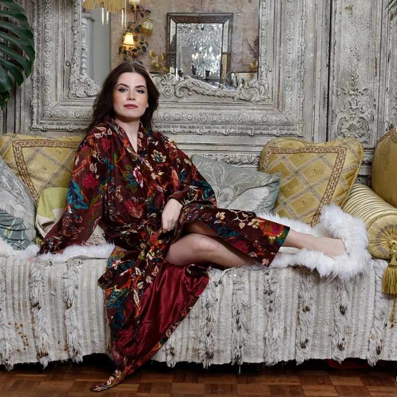 Powell Craft Velvet burgundy floral naisten puuvillainen kimono-aamutakki antiikkisen sohvalla sivuttain istuvan tummahiuksisen naisen yllä. 
