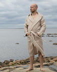Hiekansävyiseen Keltainen designin vohvelikylpytakkiin pukeutunut mies tuijottelee merenrannalla kaukaisuuteen.