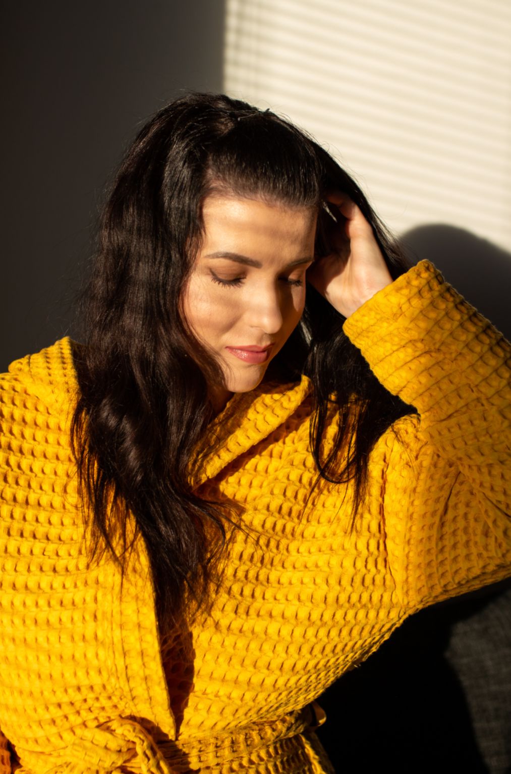 Tummahiuksinen nainen nautiskelee auringonvalosta okrankeltainen Keltainen designin vohvelikylpytakki päällään.