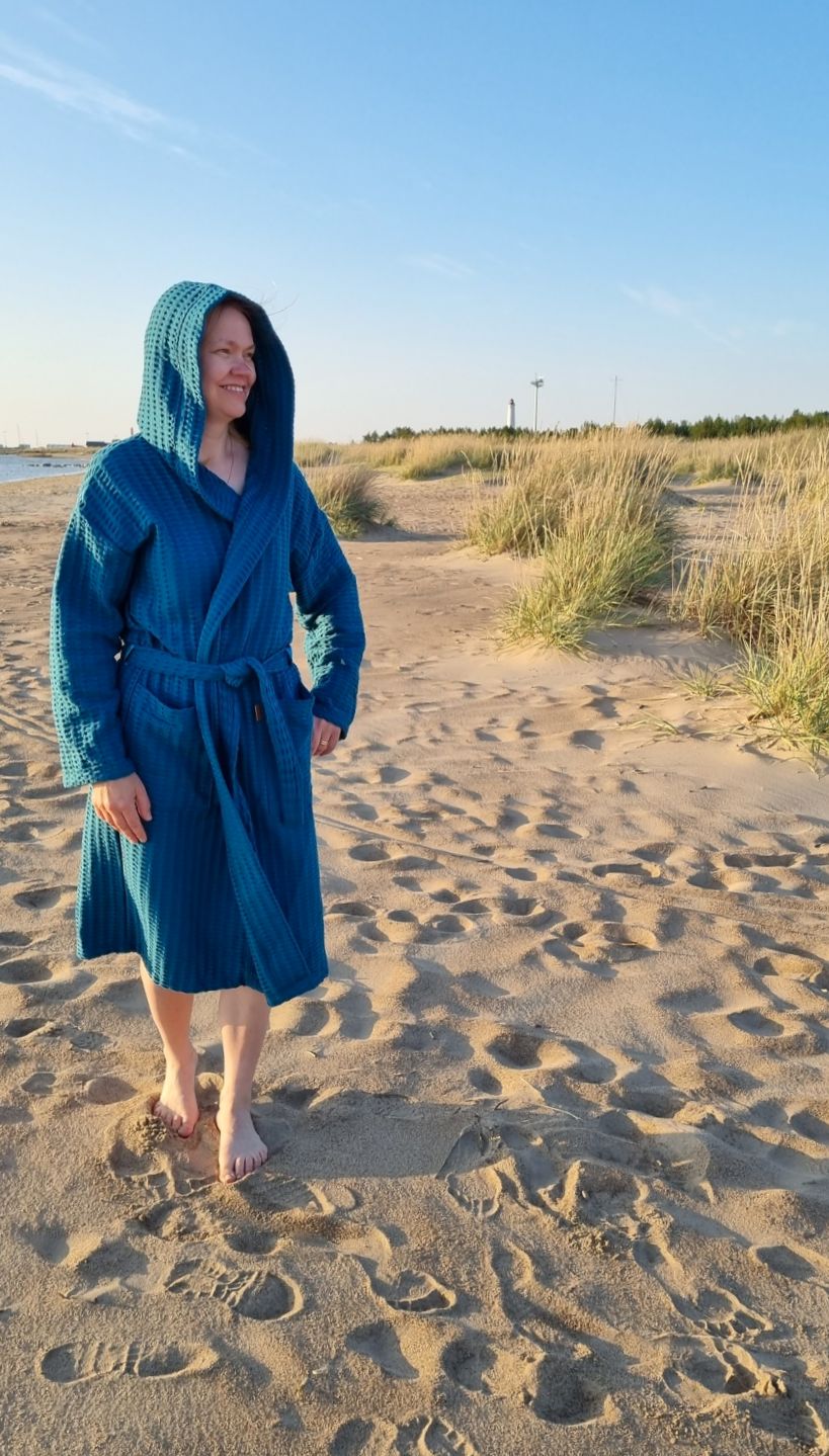 Nainen käyskenetee rantahiekalla Keltainen designin petrooli vohvelikylpytakki päällään.