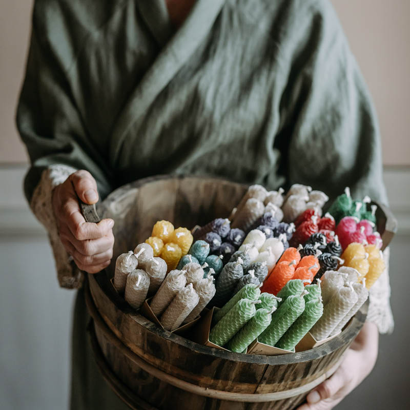 Kiulullinen toinen toistaan kauniimman värisiä Kaurilan saunan mehiläisvahakynttilöitä vihreään pellavaiseen aamutakkiin pukeutuneen naisen käsissä.