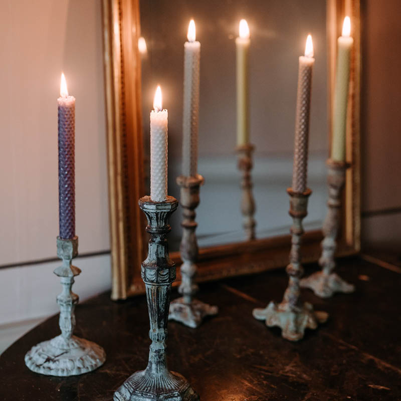 Kauniisti palavia luonnollisen säyisiä Kaurilan saunan mehiläisvahakynttilöitä rustiikkisissa metallisissa jaloissa tummalla puupöydällä, peilin edessä.