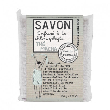 Mas du Roseaun matchantuoksuinen 100 gramman palasaippua kangas- ja paperikääreessä, jossa piirretty kuva naisesta pyyhe päällä ja ranskankielistä tekstiä.